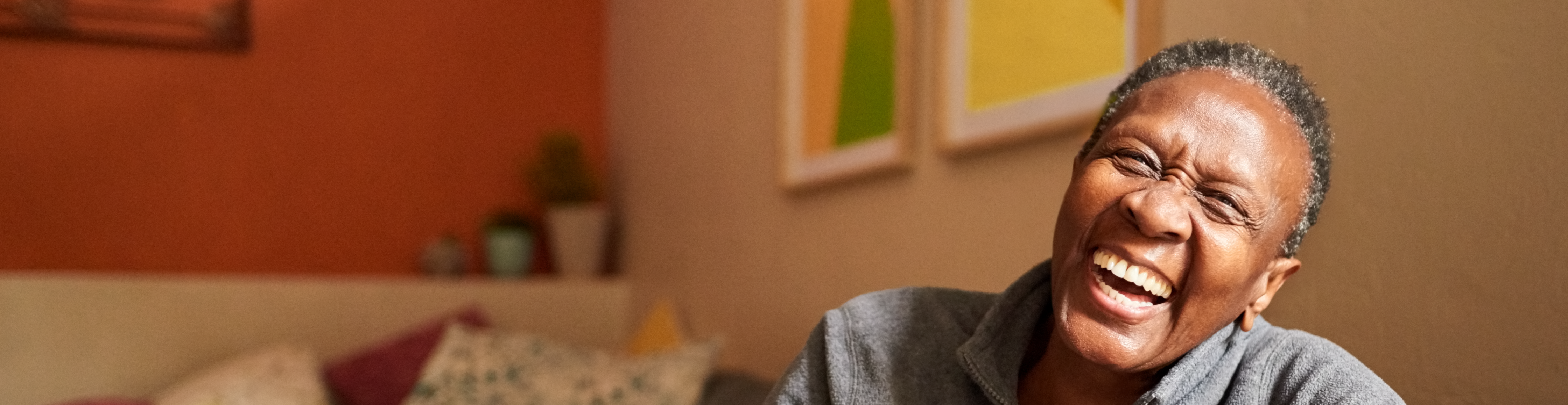 An older male sitting on a brown couch and smiling.